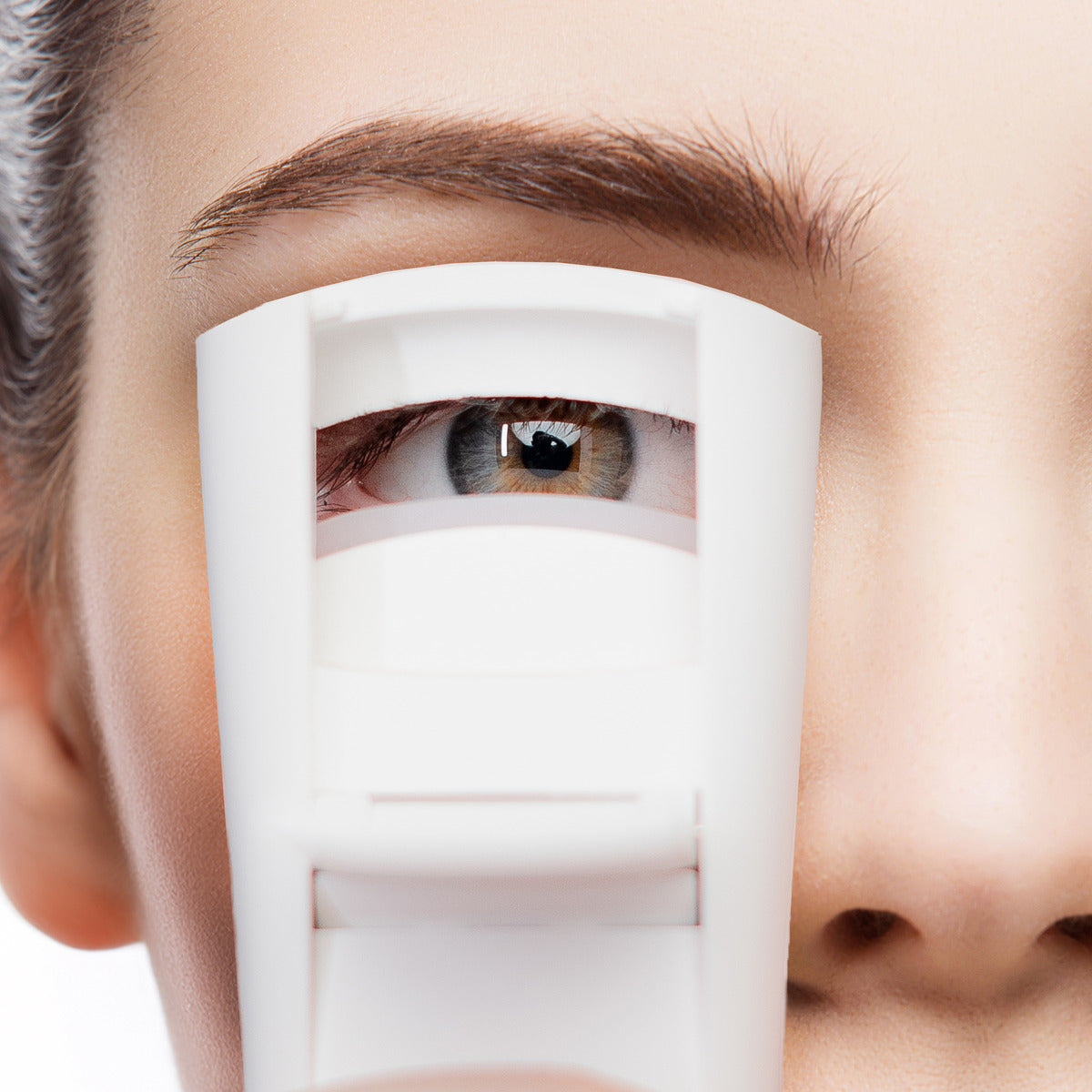 A close-up of a woman using the Wow Lash Pro Heated Eyelash Curler. The Heated Eyelash Curler is positioned on the lashes, preparing for a curl, with the woman’s eye in clear focus.