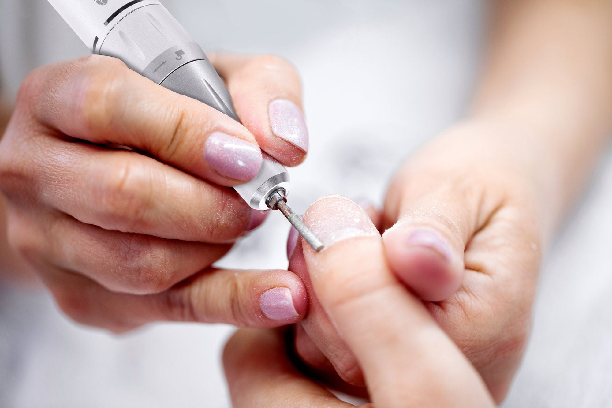 electric nail file being used by a professional to file thumb nail cuticle
